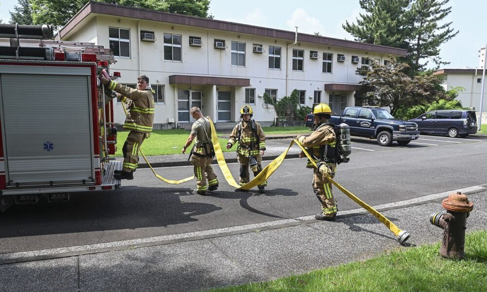 Firefighters in protective gear carrying out a training exercise with hoses in a city training yard.