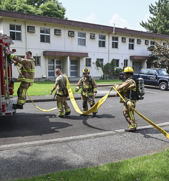 Firefighters in protective gear carrying out a training exercise with hoses in a city training yard.