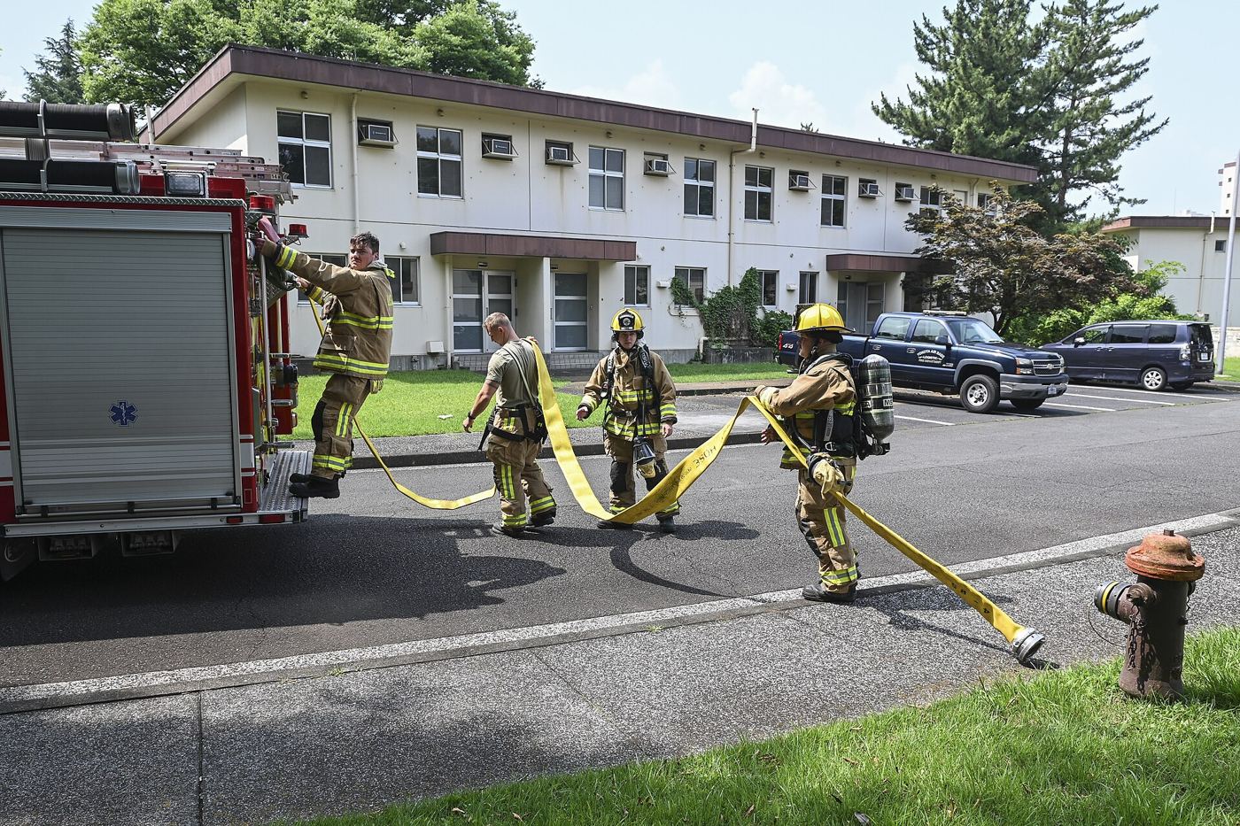 Firefighters in protective gear carrying out a training exercise with hoses in a city training yard.